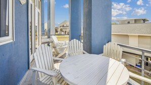 A balcony with white chairs and a table, overlooking a residential area with houses and a clear sky. - Pirates' Castle by Ryson Vacation Rentals (Galveston)