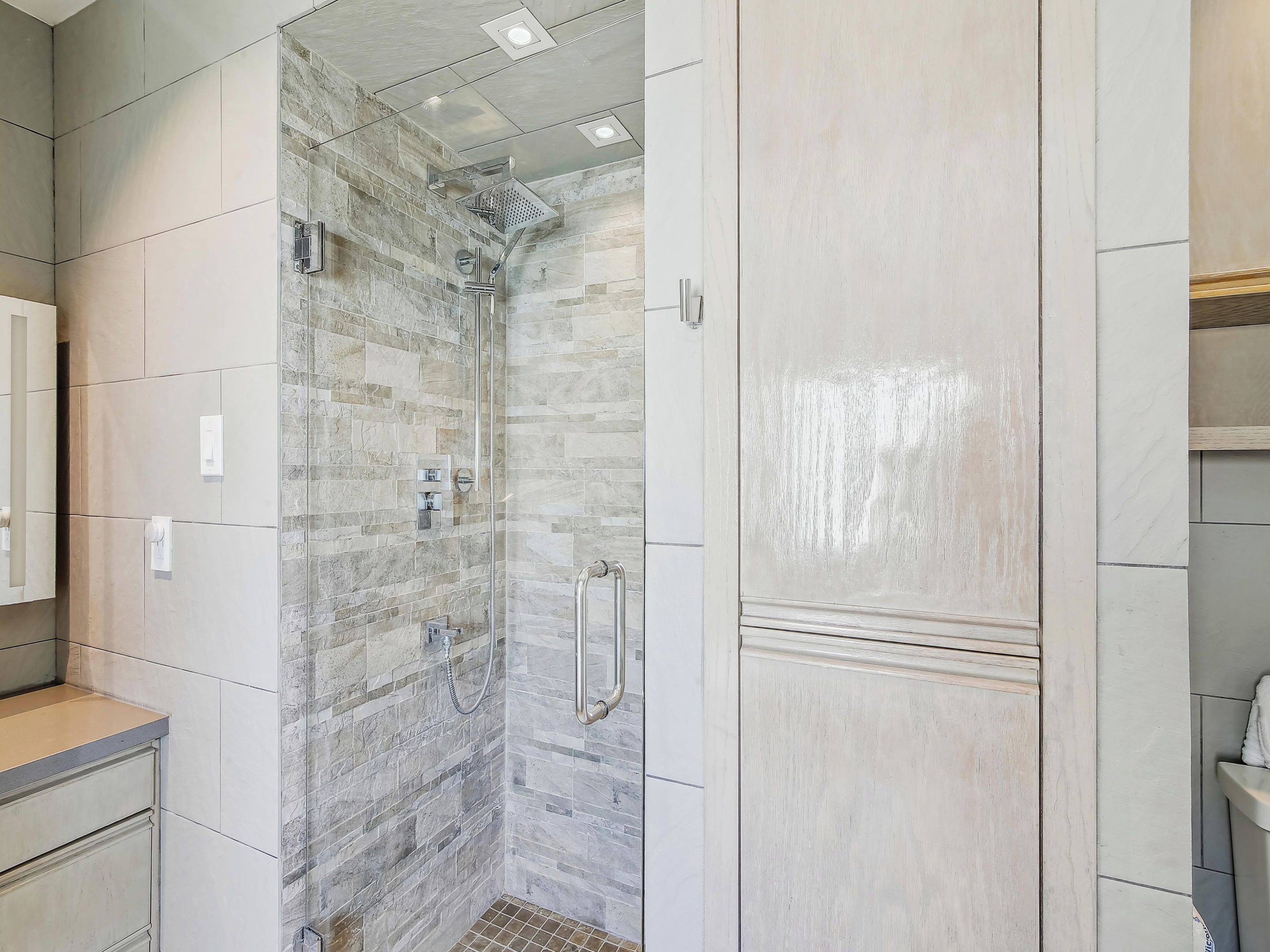 A bathroom with a shower, tiled walls, and a vanity with a mirror.