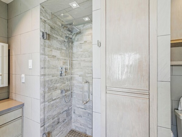 A bathroom with a shower, tiled walls, and a vanity with a mirror. - Pirates' Castle by Ryson Vacation Rentals (Galveston)