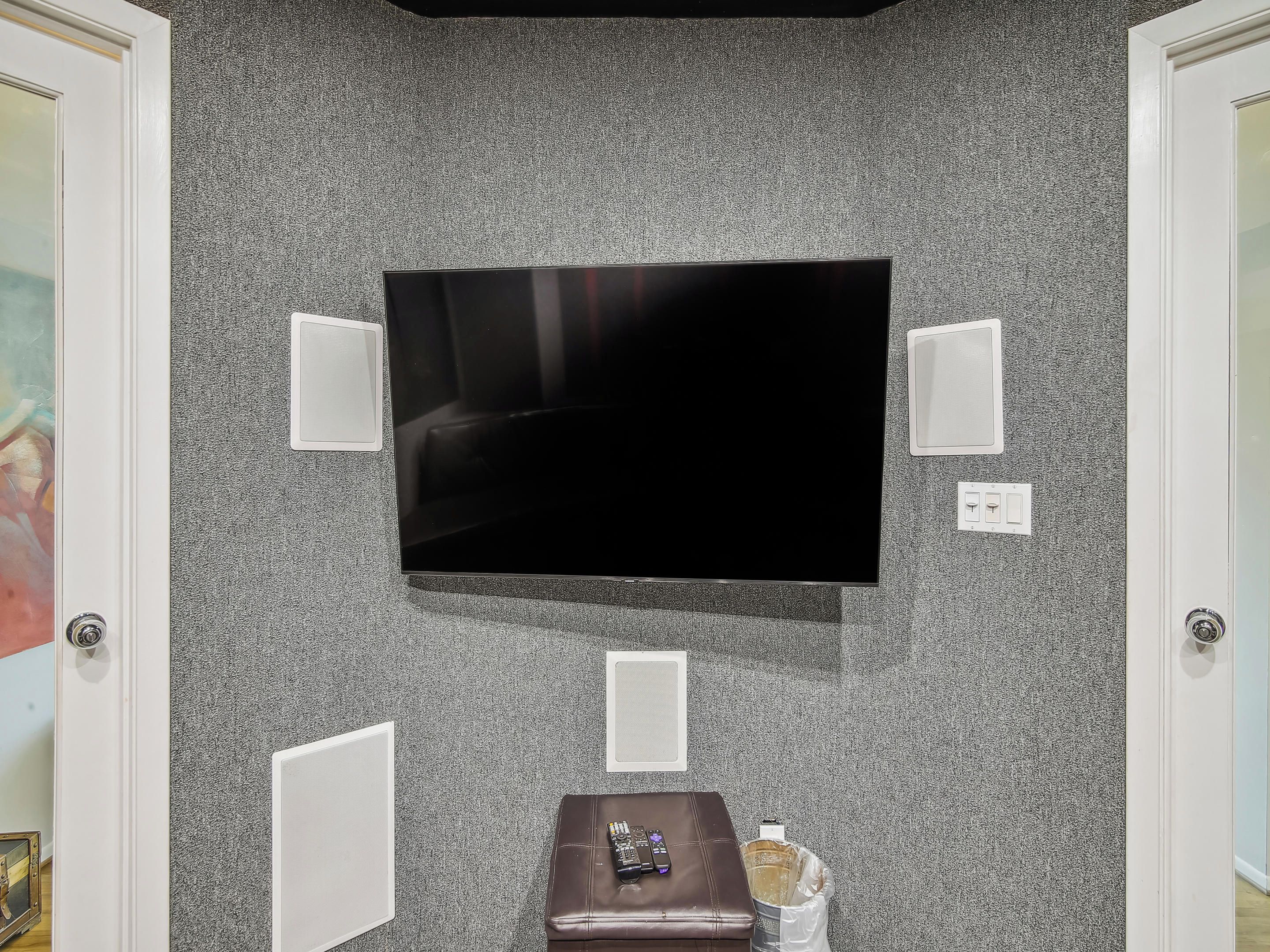 A room with a large flat-screen TV mounted on a textured gray wall, flanked by two white wall sconces.