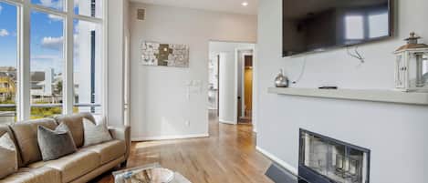 A modern living room with a leather sofa, glass coffee table, fireplace, and a large TV mounted on the wall.