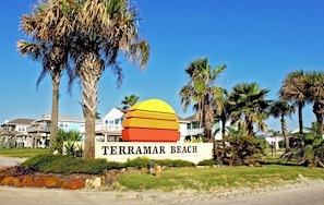 A sign for Terramar Beach with palm trees and houses in the background. - Sandy Smiles by Ryson Vacation Rentals (Galveston)