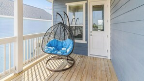 Una terraza de madera con una silla colgante azul y una puerta blanca.