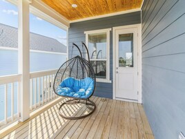 Una terraza de madera con una silla colgante azul y una puerta blanca.