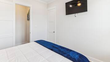 A bedroom with a bed, a TV mounted on the wall, and a door leading to another room.