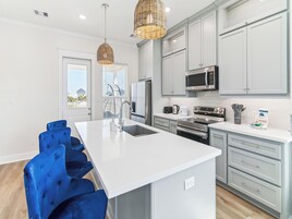A modern kitchen with white cabinetry, stainless steel appliances, and a large island with blue chairs.