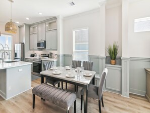 Una cocina moderna con gabinetes grises, una isla central y una zona de comedor con una mesa dispuesta para cuatro.