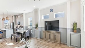 Una cocina amplia con electrodomésticos modernos, un comedor con mesa de mármol y un televisor de pantalla plana grande montado en la pared.