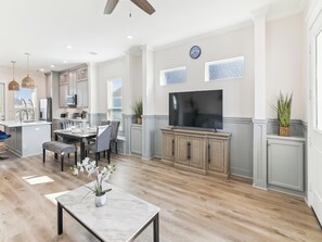 A spacious kitchen with modern appliances, a dining area with a marble table, and a large flat-screen TV mounted on the wall.