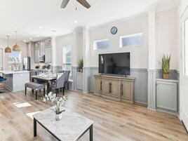 A spacious kitchen with modern appliances, a dining area with a marble table, and a large flat-screen TV mounted on the wall.