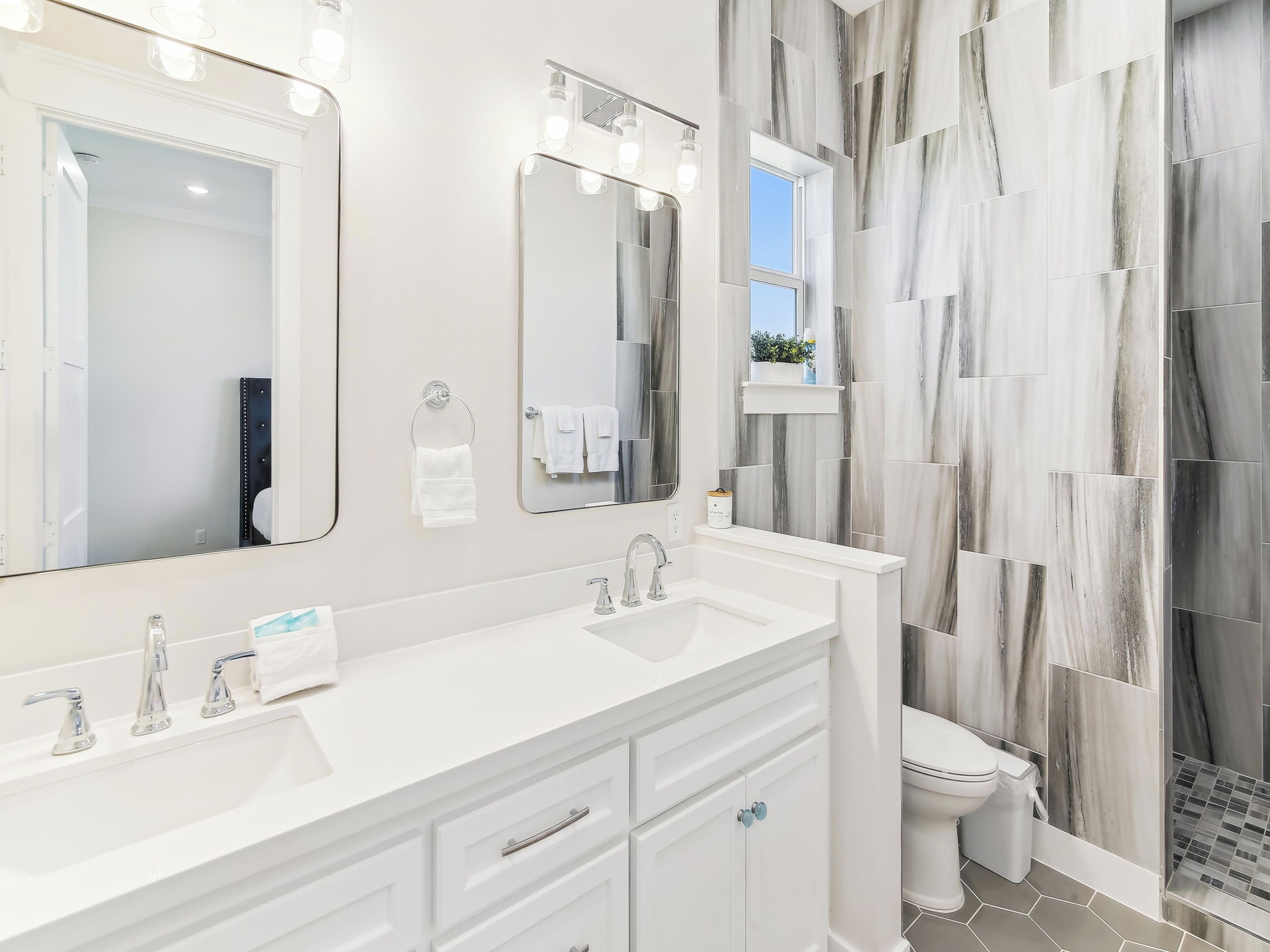 A modern bathroom with two sinks, a toilet, and a large mirror.