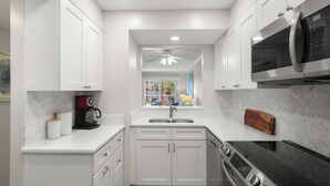 Una cocina moderna con armarios blancos, estufa de acero inoxidable, microondas y ventana con vistas al exterior.