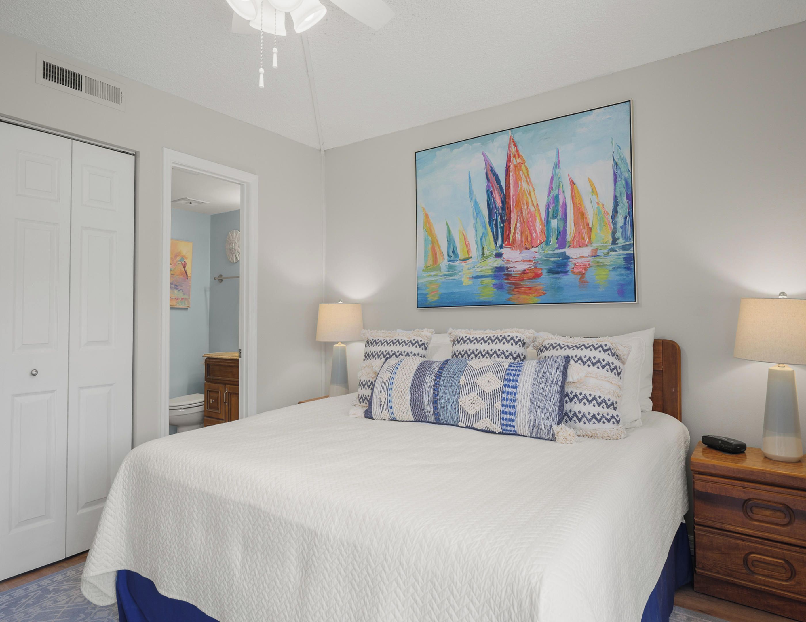 A bedroom with a bed, two bedside tables, a painting, and a door.