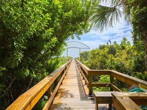 A wooden boardwalk leading to a metal gate surrounded by lush greenery. - Beach & Tennis 217 by Distinctive Beach Rentals (St. Augustine)