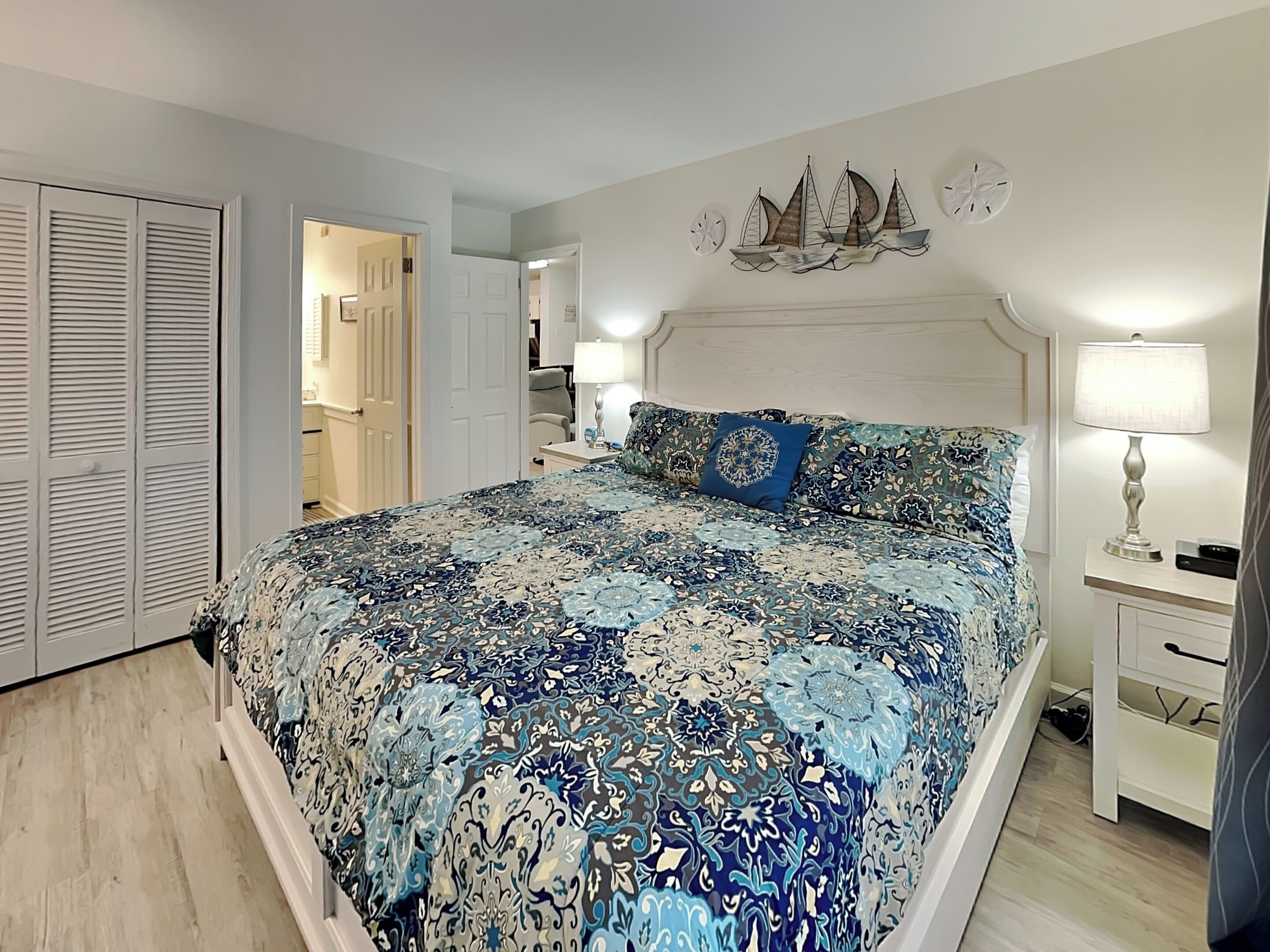 A bedroom with a large bed, a nightstand, a lamp, and a wall clock.