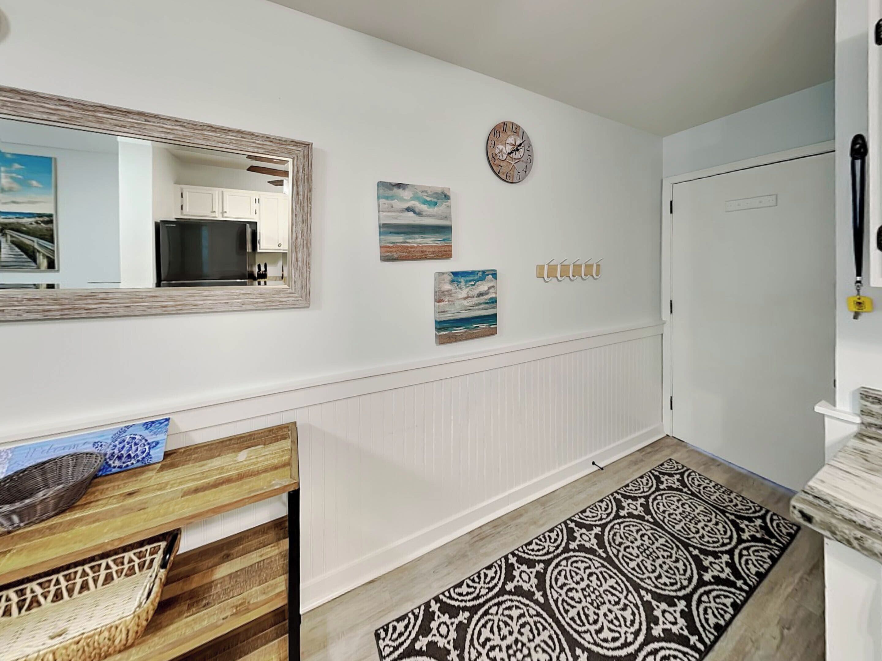 A hallway with a wooden bench, a patterned rug, a mirror, and wall-mounted artwork.