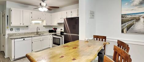 Una cocina con gabinetes blancos, un refrigerador de acero inoxidable, una mesa de comedor de madera y un ventilador de techo.