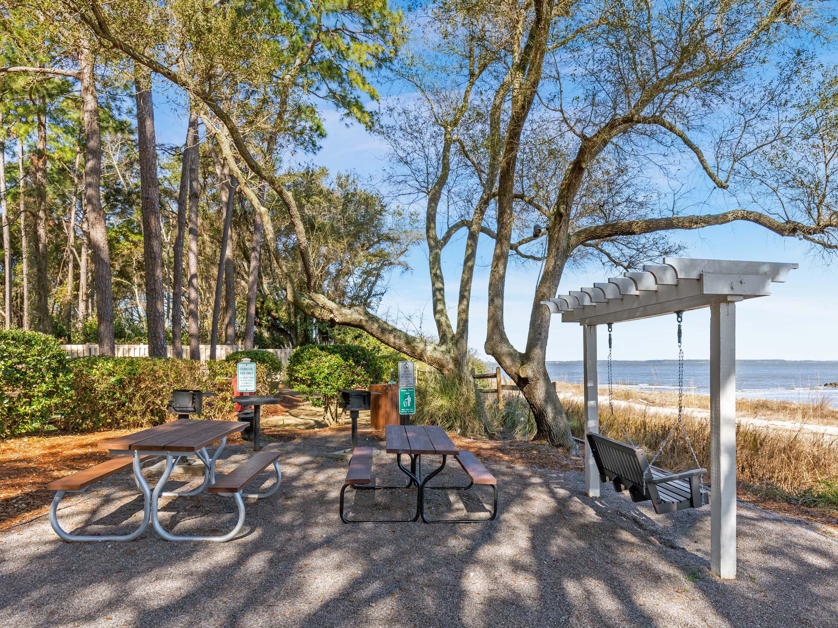 A picnic area with tables and benches, a pergola, and a view of the beach.