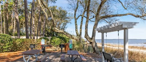 A picnic area with tables and benches, a pergola, and a view of the beach.