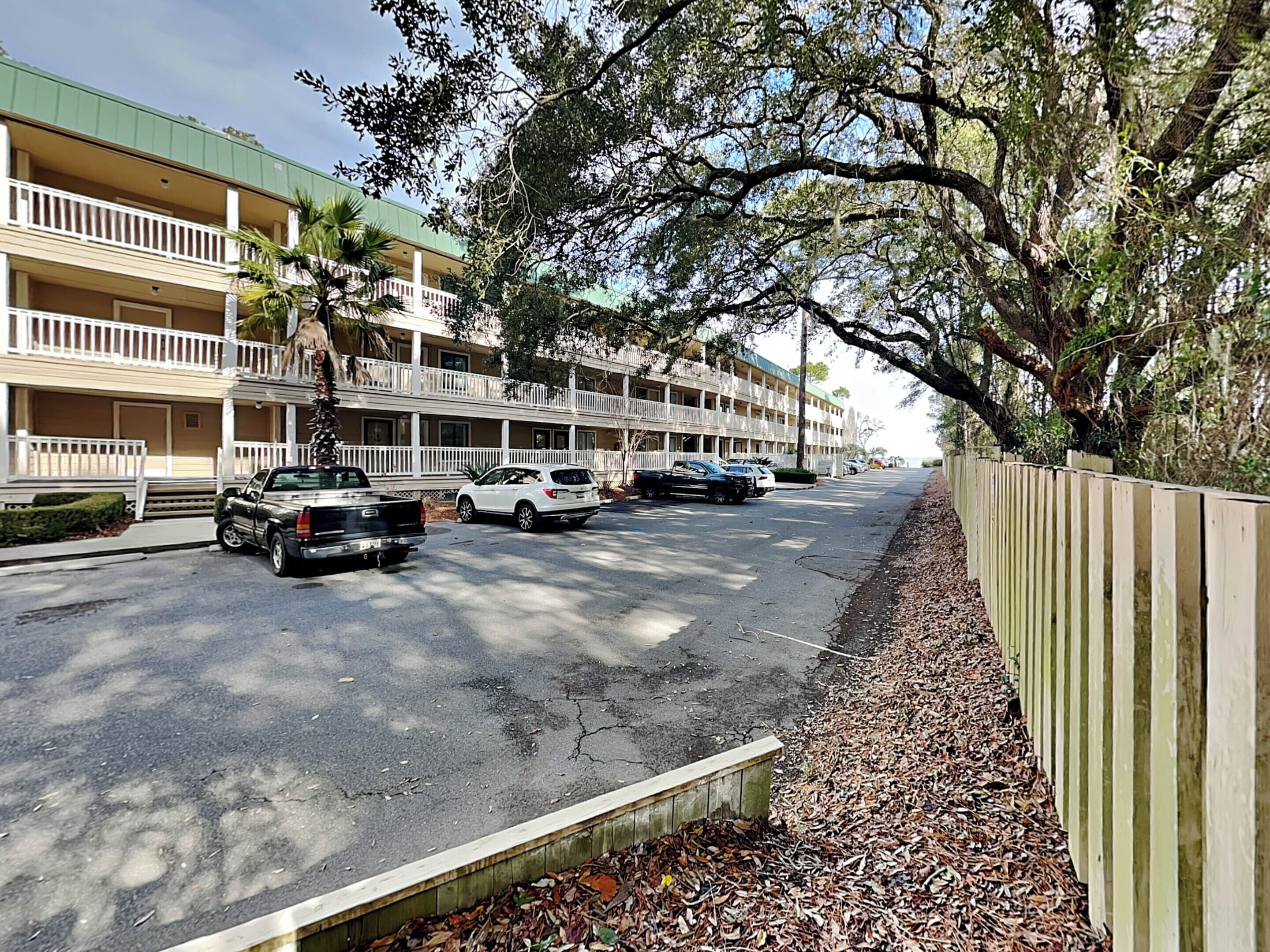 A street view with a row of two-story buildings, parked cars, and a wooden fence.