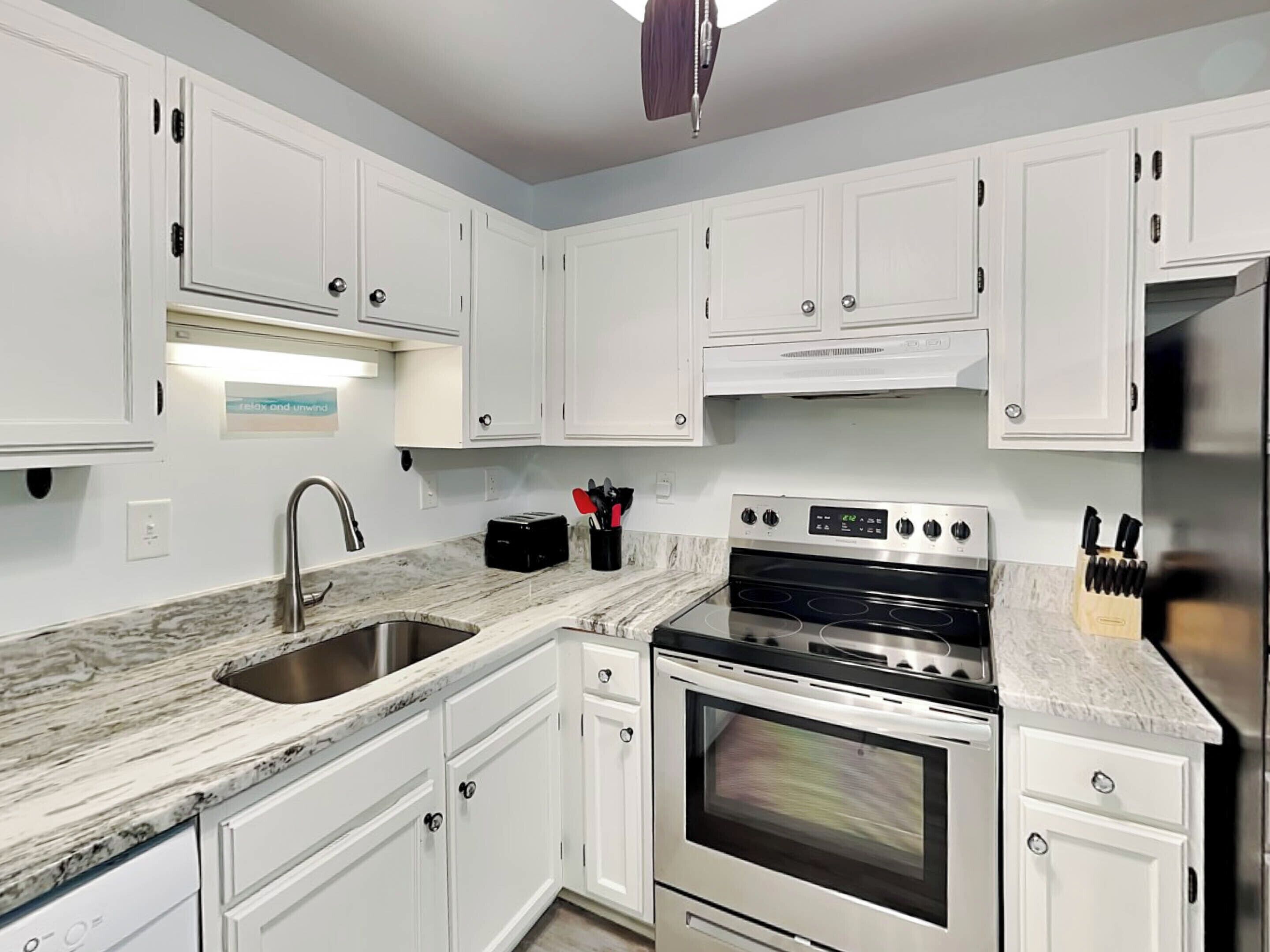 A modern kitchen with white cabinets, a stainless steel sink, a built-in oven, and a microwave.