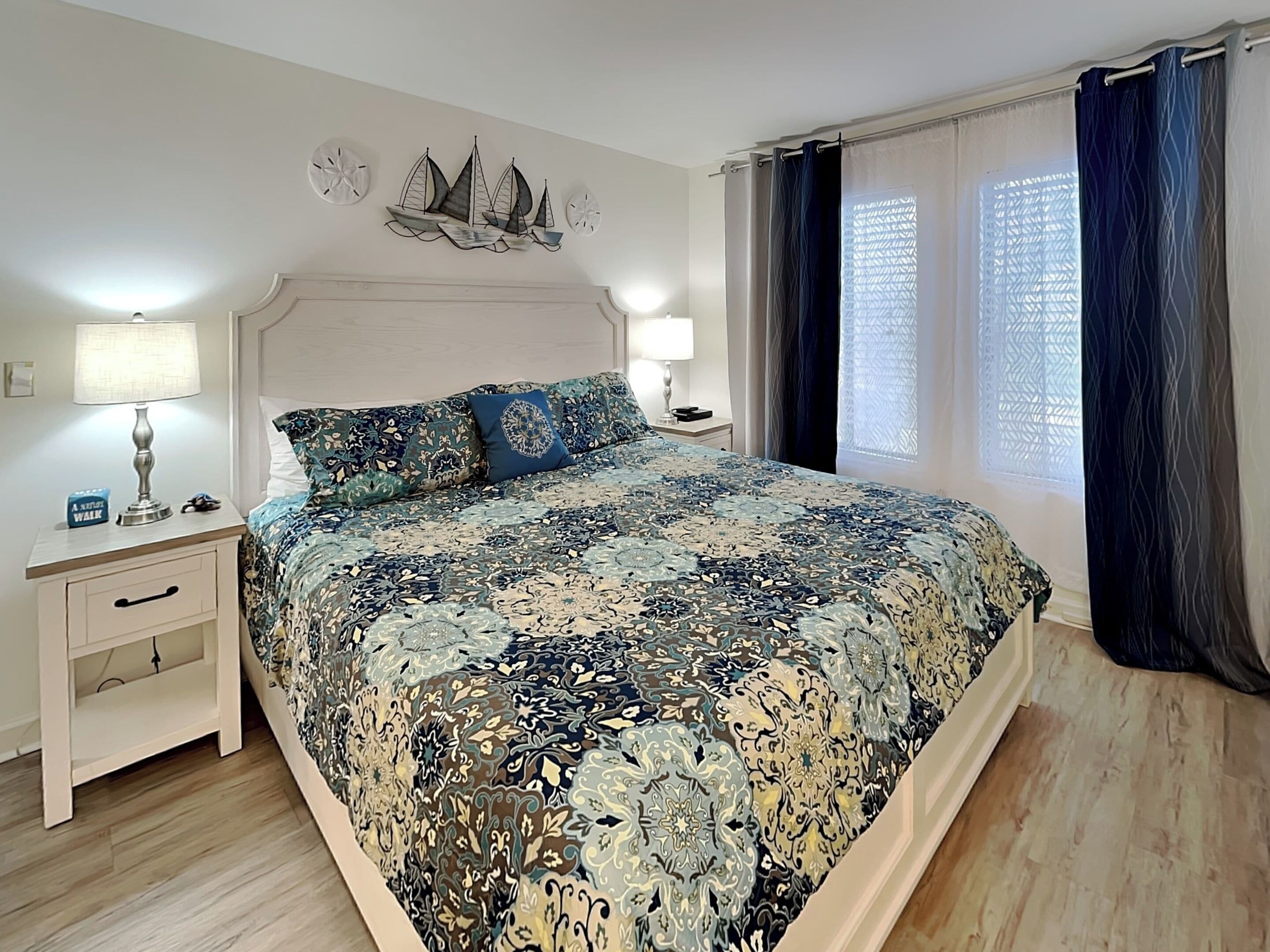 Slaapkamer met een groot bed, twee nachtkastjes, een wanddecoratie en een raam met gordijnen.