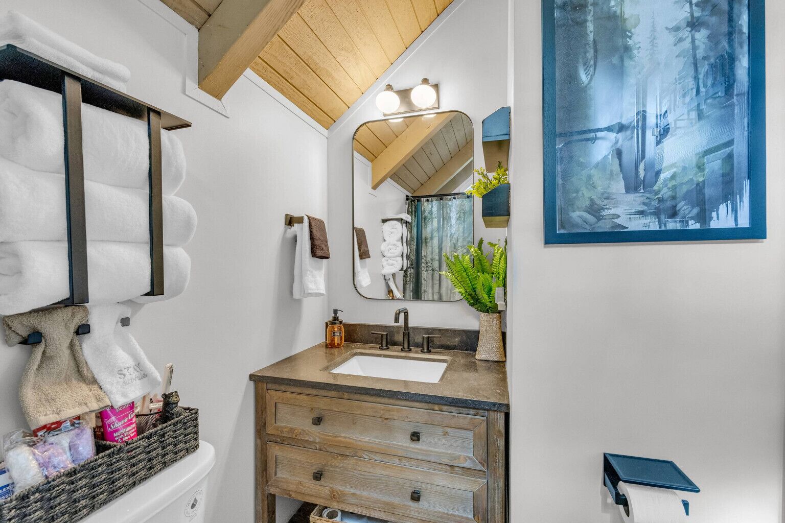 Un bagno con un mobile vanitario in legno, un grande specchio e un dipinto raffigurante una scena forestale.