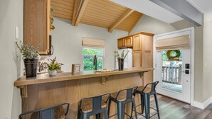 A kitchen with a wooden bar and stools, a window with a view, and a door with a wreath.