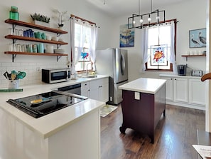 A modern kitchen with white cabinetry, a central island, stainless steel appliances, and decorative elements like plants and artwork.