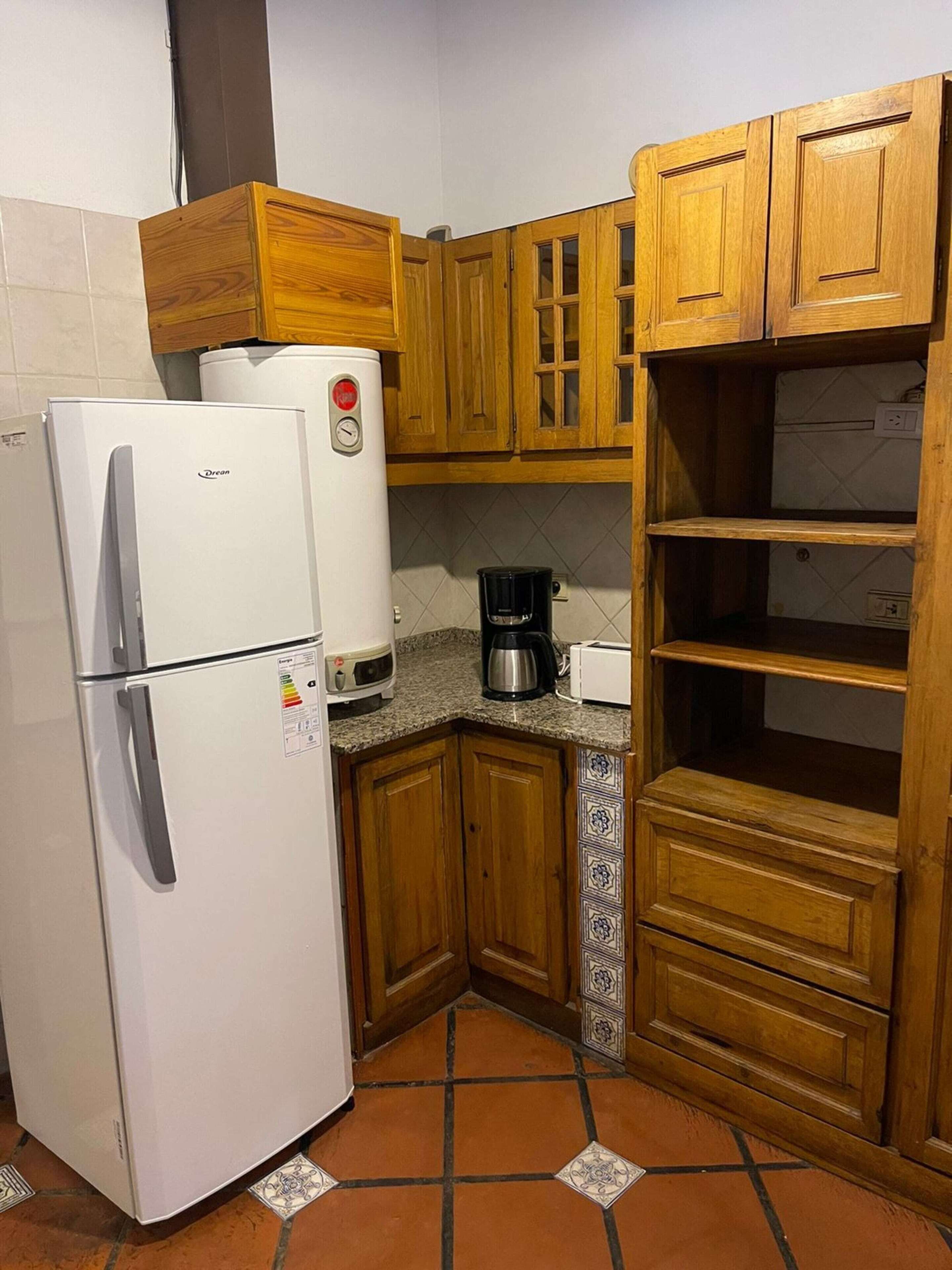 A compact kitchen with wooden cabinets, a white refrigerator, a coffee maker, and a tiled backsplash.