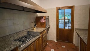 A compact kitchen with a gas stove, wooden cabinets, and a tiled backsplash. - Casa Loria by Vilvey Turismo (Chacras de Coria)