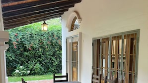 A patio with a wooden table and chairs, a tiled floor, and a view of a garden with a hedge and flowers. - Casa Loria by Vilvey Turismo (Chacras de Coria)