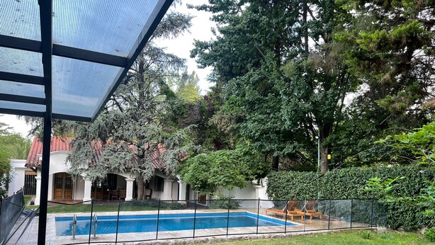 A backyard with a swimming pool, surrounded by lush greenery and a house with a red-tiled roof. - Casa Loria by Vilvey Turismo (Chacras de Coria)