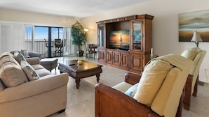 A spacious living room with a large TV, comfortable seating, a dining area, and a balcony with a view. - Reflections on the Gulf by Distinctive Beach Rentals (Indian Rocks Beach)