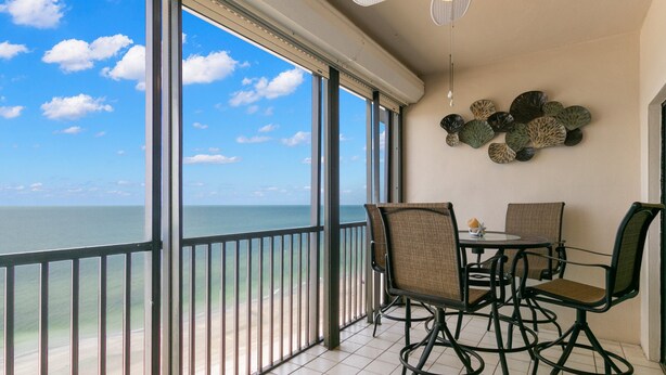 A balcony with a view of the ocean, a ceiling fan, and a table with chairs. - Reflections on the Gulf by Distinctive Beach Rentals (Indian Rocks Beach)