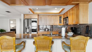 A modern kitchen with wooden cabinets, stainless steel appliances, and a bar area with wicker chairs. - Reflections on the Gulf by Distinctive Beach Rentals (Indian Rocks Beach)