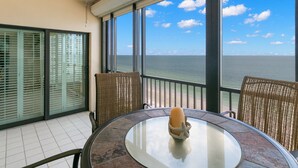 A balcony with a glass table, wicker chairs, and a ceiling fan. - Reflections on the Gulf by Distinctive Beach Rentals (Indian Rocks Beach)