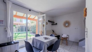 Een kamer met een tafel en stoelen, een klein krukje, een bank buiten, en een schuifdeur die leidt naar een tuin.