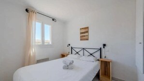 Een slaapkamer met een bed, een raam met gordijnen, een aan de muur hangend kunstwerk en nachtkastjes.