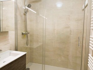 Bathroom features a glass-enclosed shower, handheld showerhead, and wall-mounted control panel.