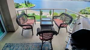 A balcony with wicker chairs, a small table, and a grill. It overlooks a lake and a golf course. - Sunset Waterfont Resort 12. Luxury Lakeside, Lakeview 3 bed/2bath Kelowna Condo. (Kelowna)