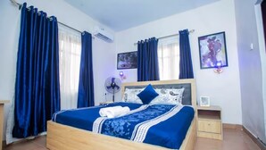 A bedroom with a wooden bed, blue curtains, a bedside table, and a wall-mounted air conditioner. - AJI (1.0) | Warm 2BED Apartment (Ijegun, Lagos) (Lagos)