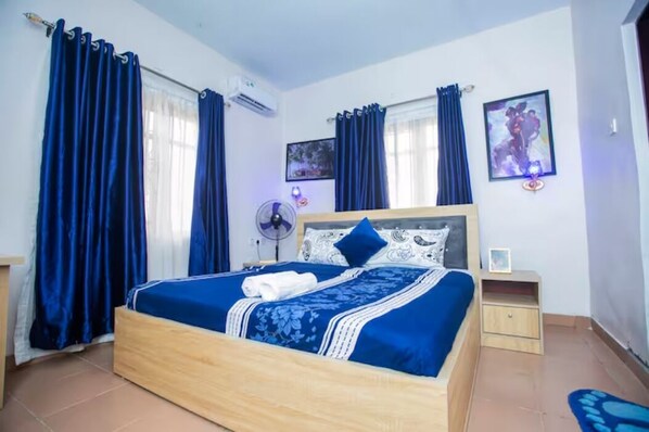 Ein Schlafzimmer mit einem hölzernen Bett, blauen Vorhängen, einem Nachttisch und einer Wand-Klimaanlage.