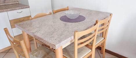 Uma pequena mesa de jantar com uma tigela de vidro sobre um jogo de sousa roxo, cercada por cadeiras de madeira com assentos acolchoados.