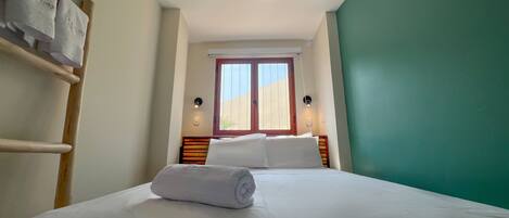 Una habitación de hotel con una cama, una ventana, un perchero en la pared y una lámpara de pared.