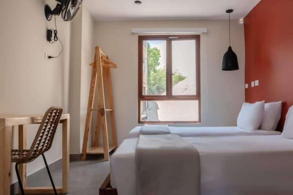 A bedroom with a bed, a desk, a chair, a ladder, and a window.