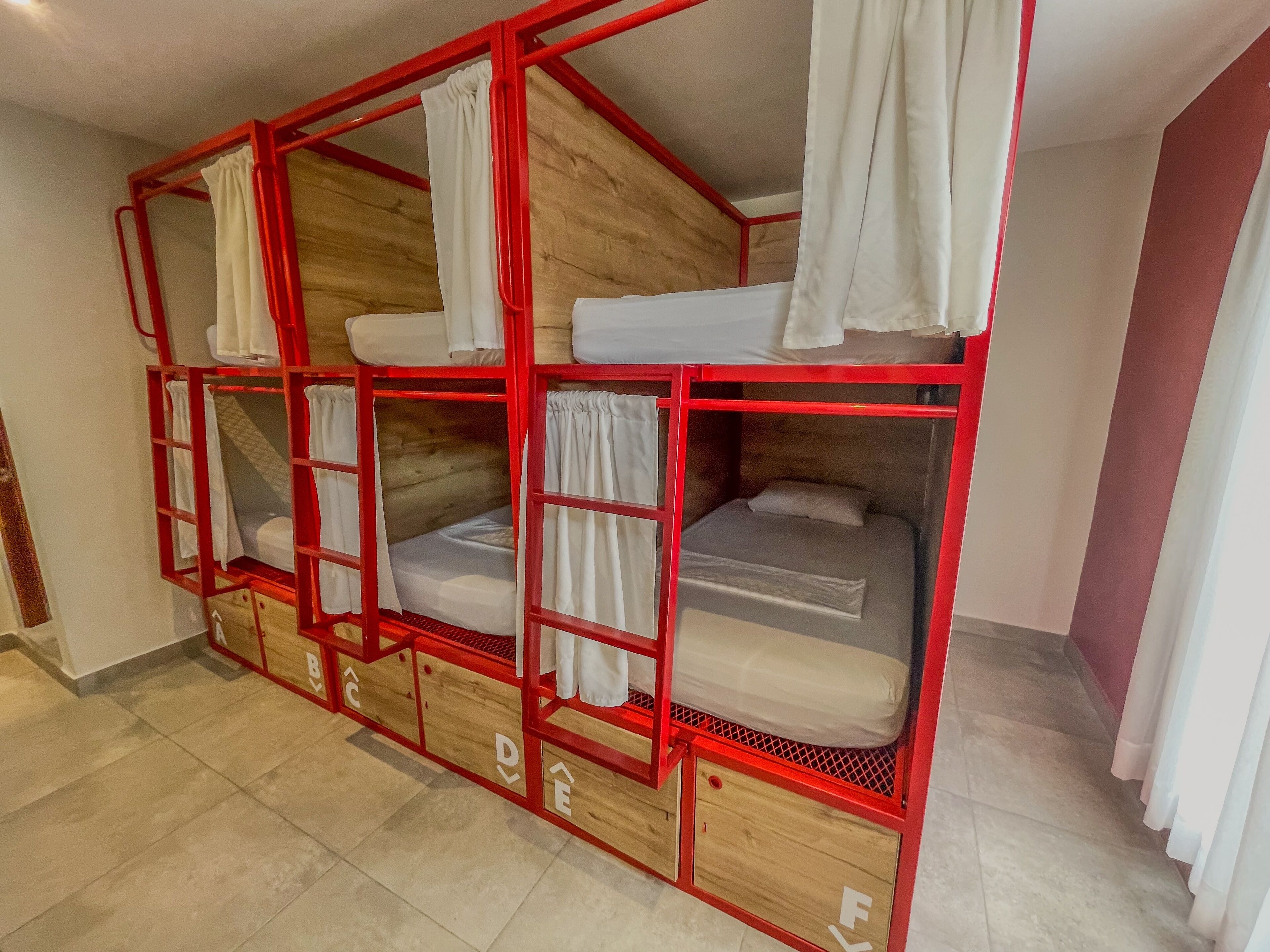 A bunk bed with a red frame and white bedding, wooden panels, and storage drawers.