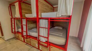 Una cama litera con estructura roja, ropa de cama blanca, paneles de madera y cajones para guardar objetos.