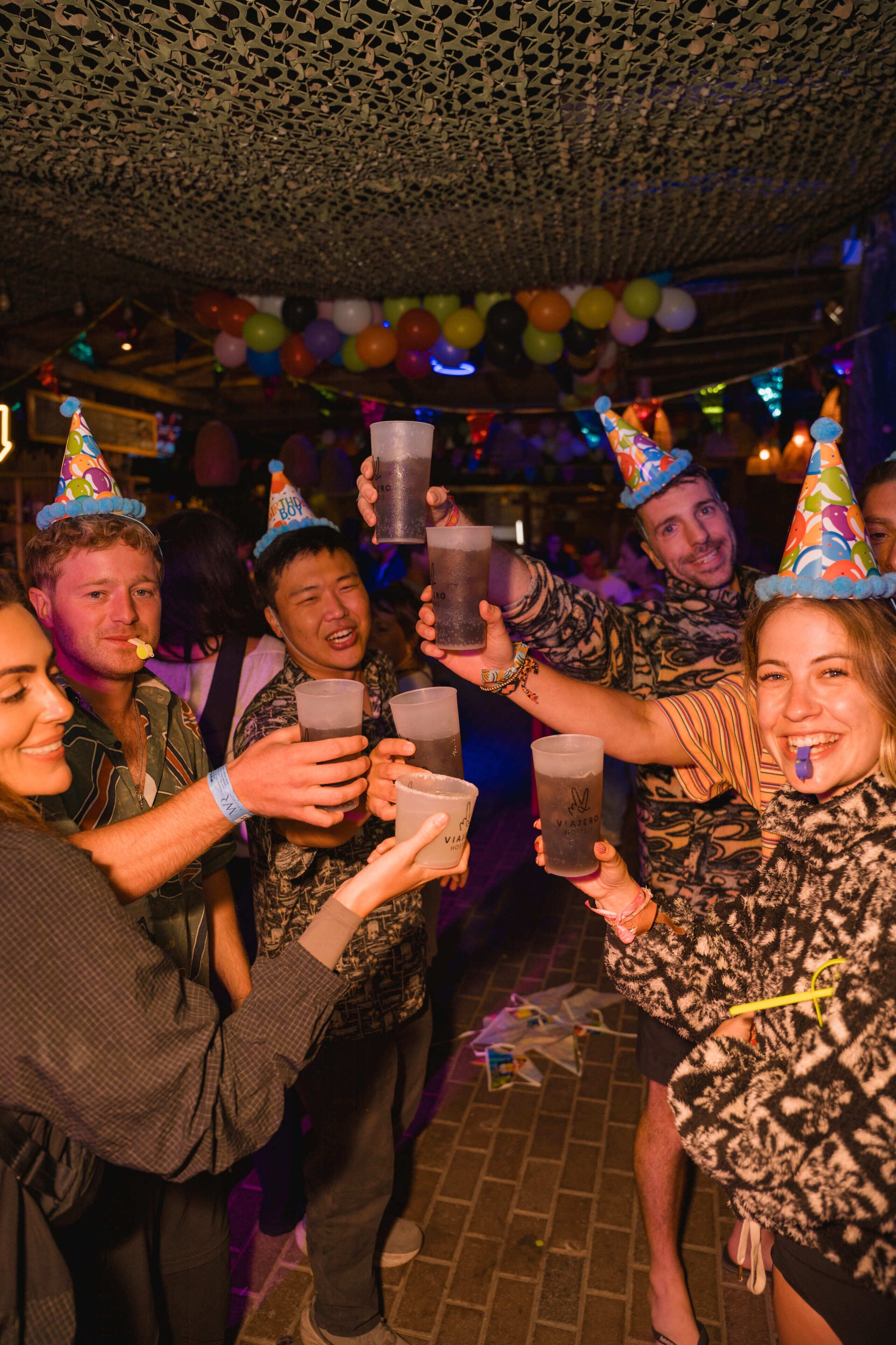Un grupo de personas en una fiesta, sosteniendo bebidas y usando gorros de fiesta.