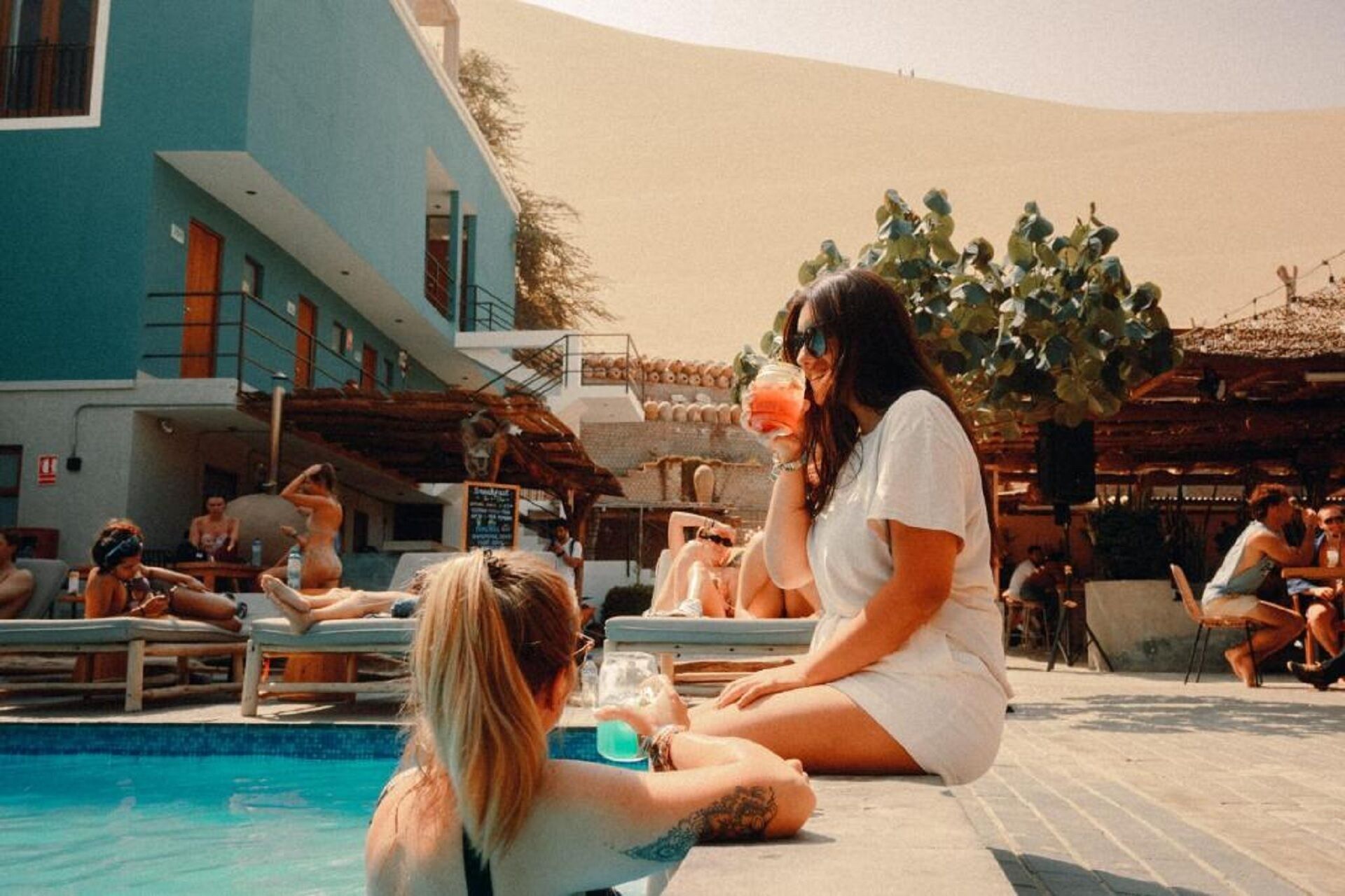 Zona junto a la piscina con piscina, sillones de descanso y un edificio de fachada azul.
